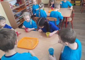 Dzieci siedzące przy dwóch stolikach bawią się bańkami mydlanymi.
